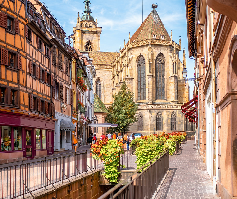 Ruelle commerçante fleurie de Colmar avec l'église Saint-Martin en arrière-plan